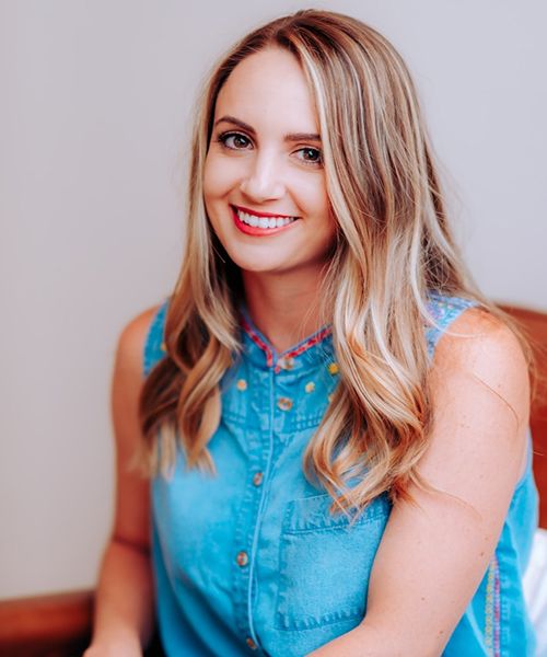 Smiling woman in denim shirt, sitting casually.