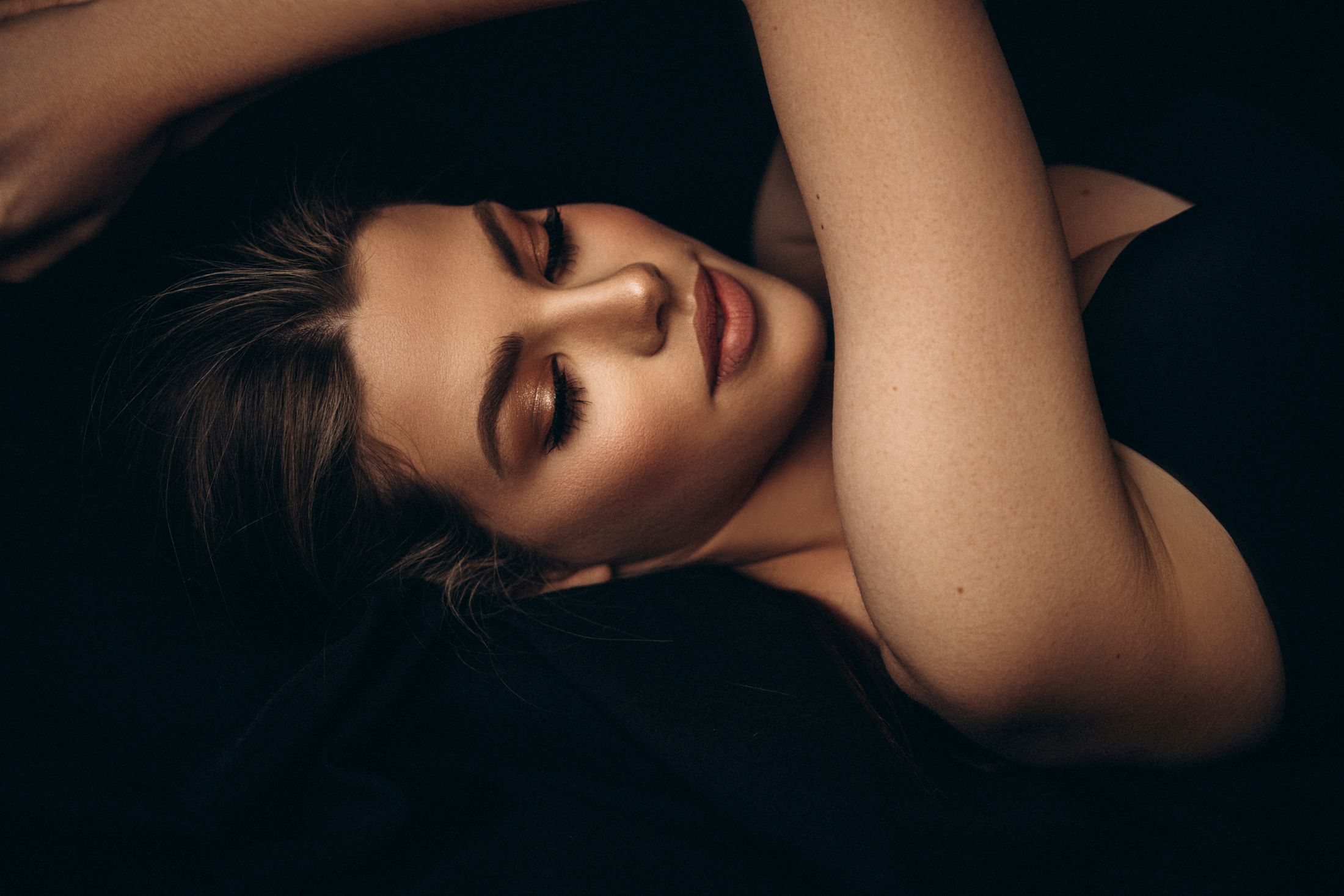 Woman with closed eyes resting on dark fabric.